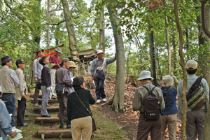 （写真）鎮守の森で木々の説明を受ける参加者