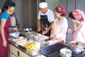 （写真）講師のアドバイスを受けながら、調理に取り組む参加者たち