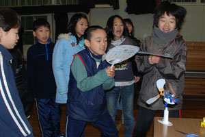（写真）うちわをおこした風で電気を作る体験を行っている小学生ら