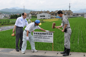 （写真）学校給食に使われる米を提供している水田に看板を立てる職員ら