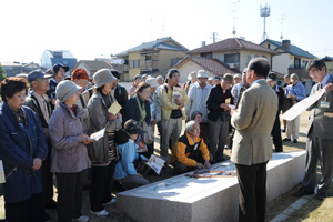 （写真）朝堂院跡の案内板を前に中尾芳治さんから説明を受ける参加者