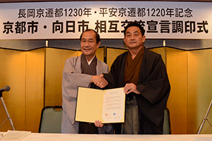 （写真）調印書を掲げ握手する門川市長と久嶋市長